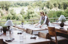 A waitress sets tables on a terrace with a view of the Donau-Auen National Park.