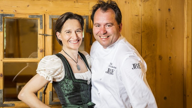 A man in a chef's jacket and a woman in traditional costume smile at the camera.