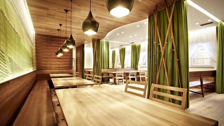 Modern restaurant with wooden tables and green curtains.