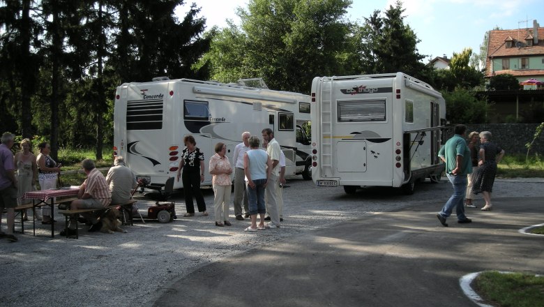 People stand and sit next to two mobile homes on an outdoor pitch.