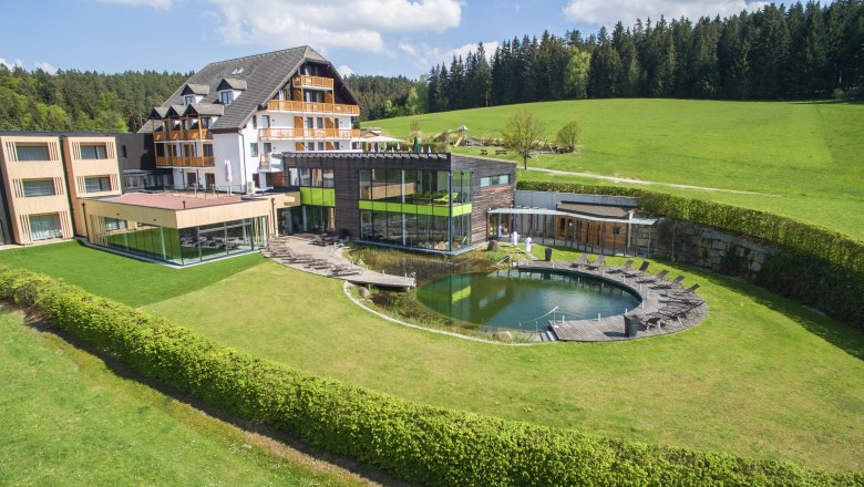 Hotel Schwarz Alm Zwettl, © Schwarz Alm Hotel Schwarz Alm Zwettl with natural pond and sun loungers, surrounded by green countryside.