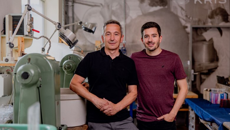 Two men are standing in a workshop with machines in the background.
