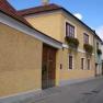 Yellow house with red roof tiles and flower boxes on the windows in a narrow street.