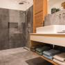 Modern bathroom with gray tiles, glass shower and wooden washbasin.