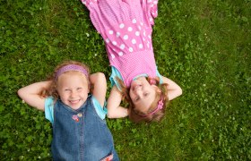 Two laughing girls lie on a meadow.