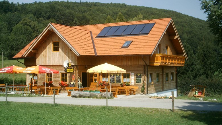A traditional inn with wooden walls and red roof tiles, surrounded by green countryside and forest.