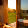 View from a room onto a terrace at sunset, with meadow and forest in the background.
