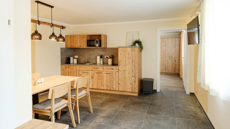 Modern kitchen with wooden furniture and dining table, bright lighting.