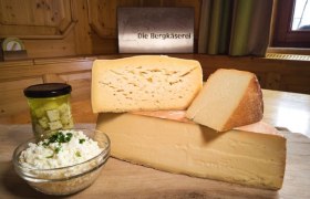 Different types of cheese on a wooden board with a jar of pickled cheese and a bowl of cream cheese.