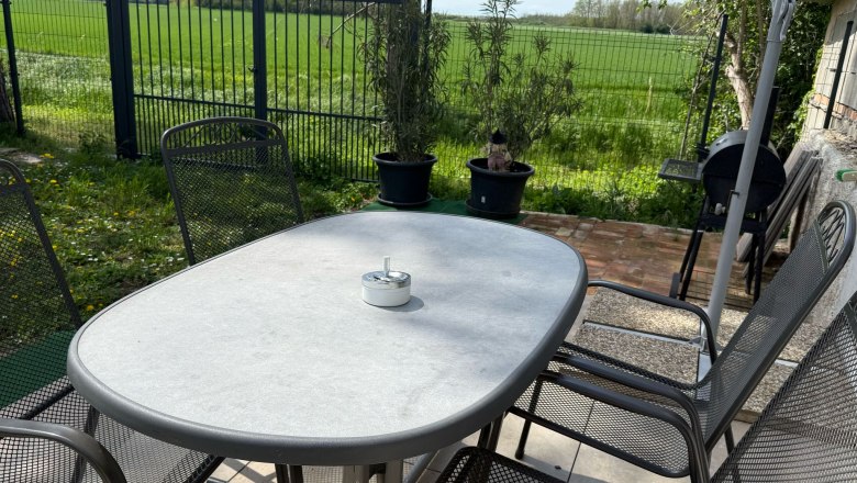 Garden table with chairs on a terrace, surrounded by green lawn and a fence.
