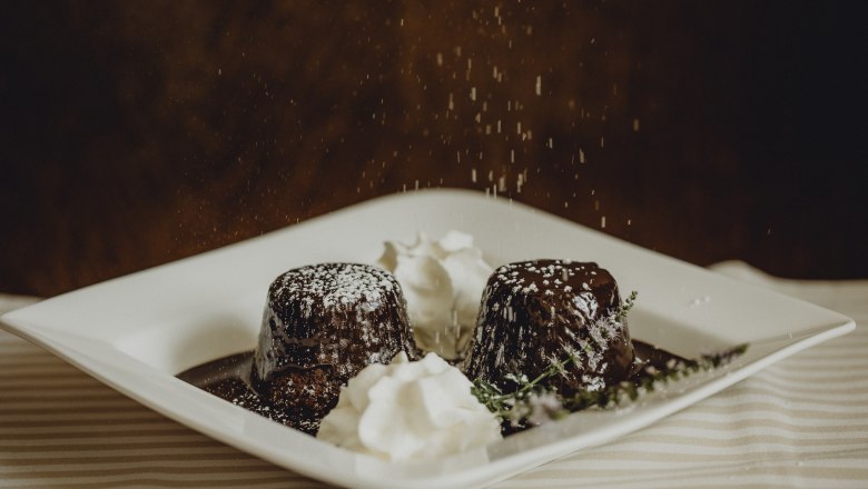Two chocolate cakes with powdered sugar and cream on a plate.