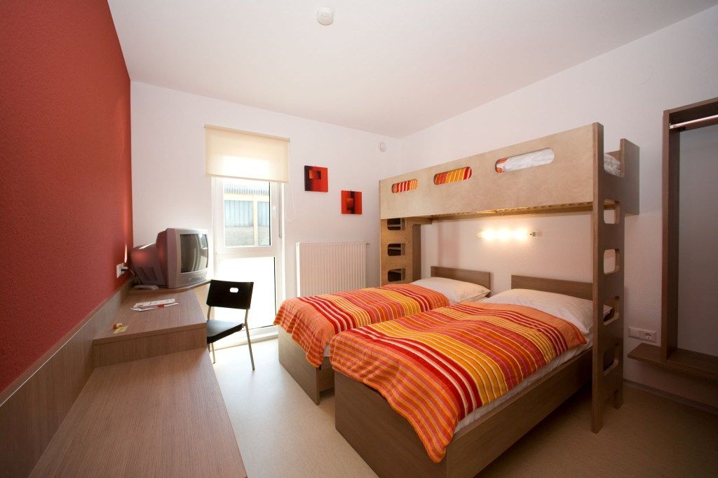 A modern room with a bunk bed, desk, chair and TV. The walls are partly painted red.