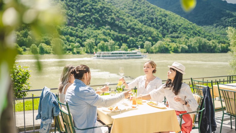 Four people sitting at a beautifully laid table on a terrace with the Danube and a ship in the background