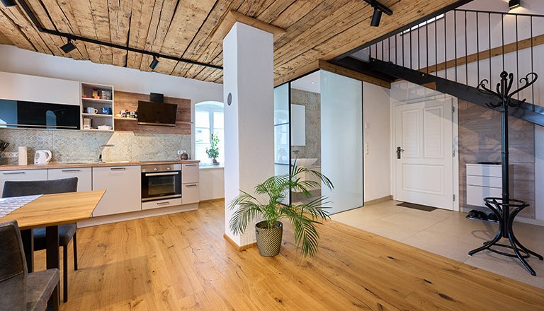 Modern kitchen with wooden floor and ceiling, staircase and plants.