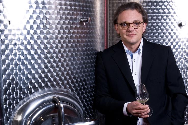 A man in a suit holds a wine glass in front of a large stainless steel tank.