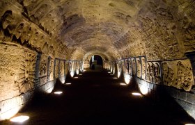An illuminated, vaulted tunnel with artistic reliefs on the walls.