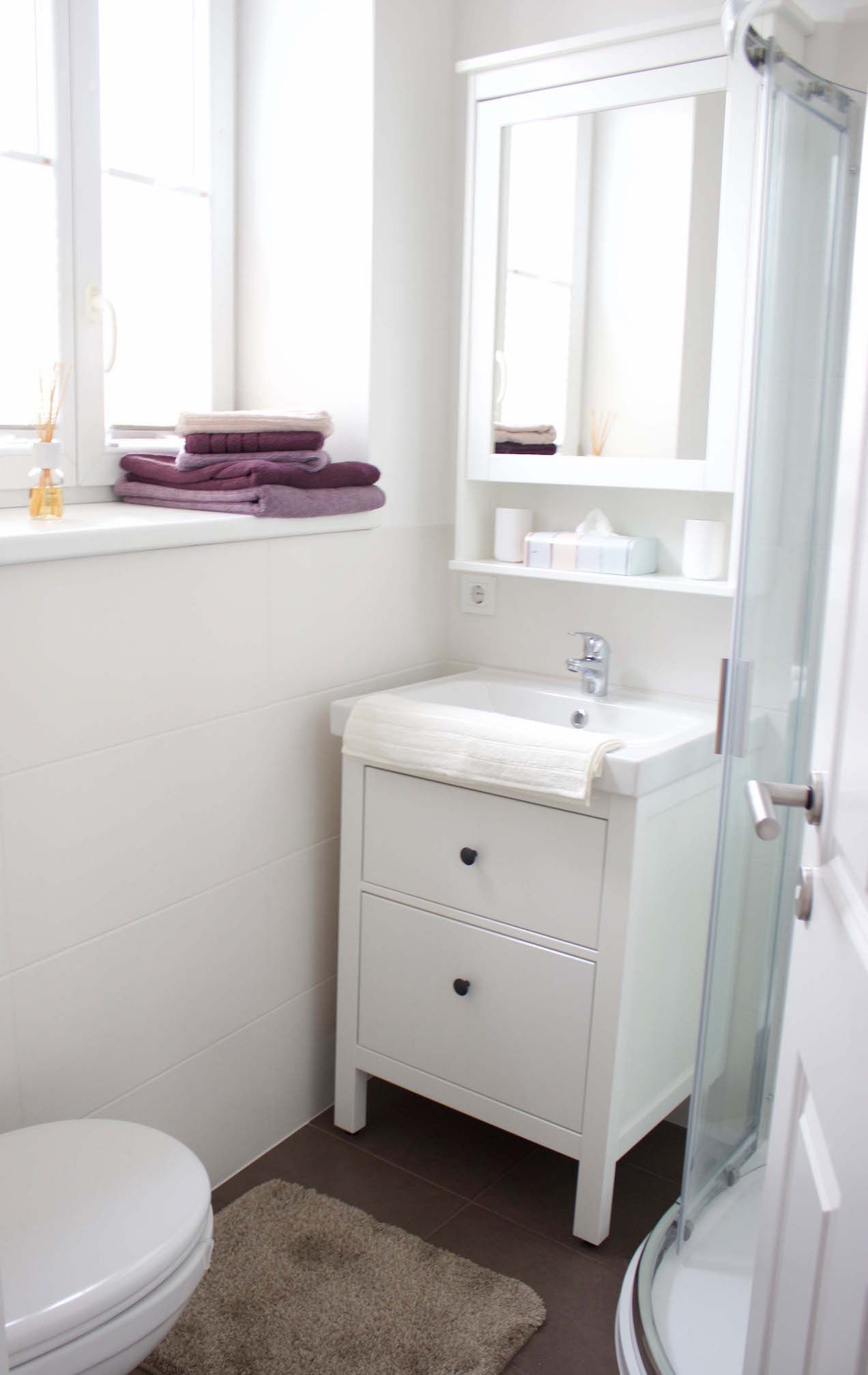 Modern bathroom with white washbasin, mirror, towels and shower.