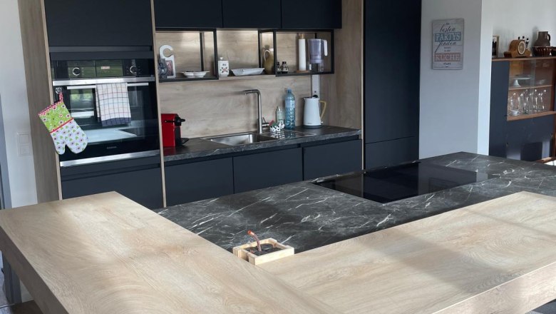 Modern kitchen with wood and marble elements, three hanging lamps and black cupboards.