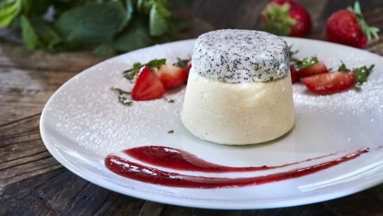 A dessert of semolina flummery topped with poppy seeds, garnished with strawberries and mint on a white plate.