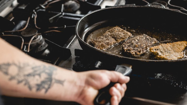 Person frying pieces of fish in a pan on a stove.