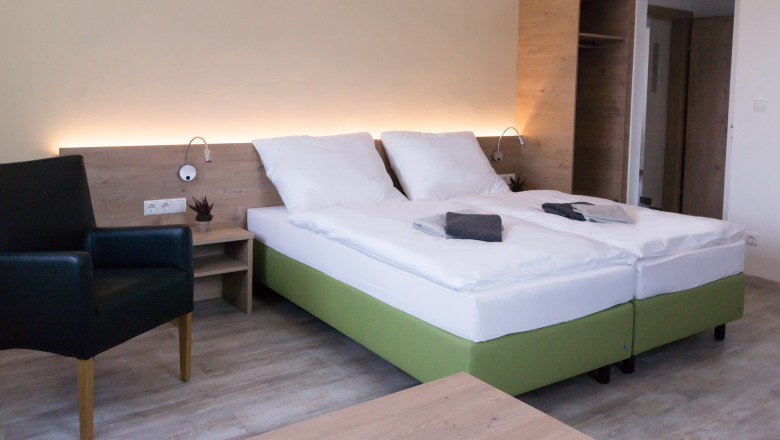 Modern furnished hotel room with double bed, bedside table, armchair and closet.