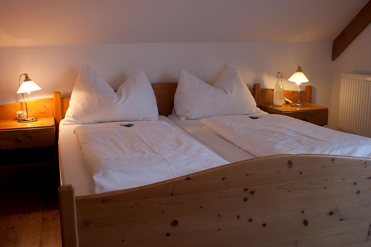 Comfortable double bed in a country inn room with wooden frame and bedside tables, illuminated by two table lamps.