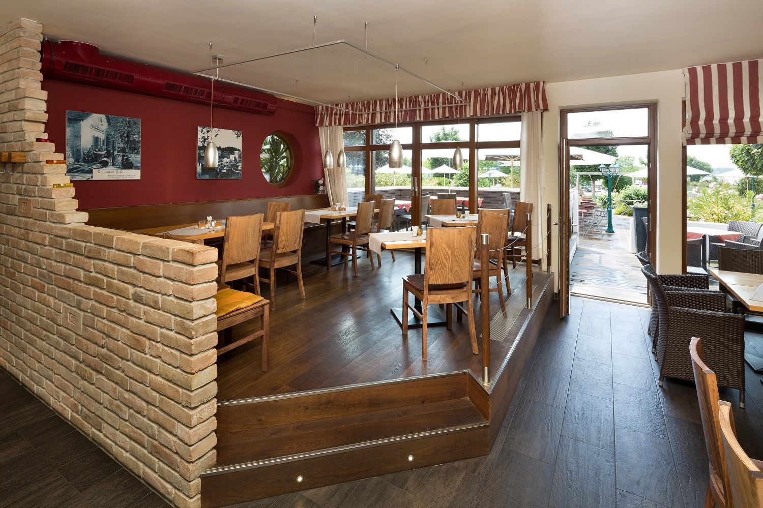 A cozy restaurant with wooden furniture, red walls and large windows leading onto a terrace.