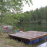 A quiet lake with a wooden jetty and several canoes on the shore, surrounded by trees.