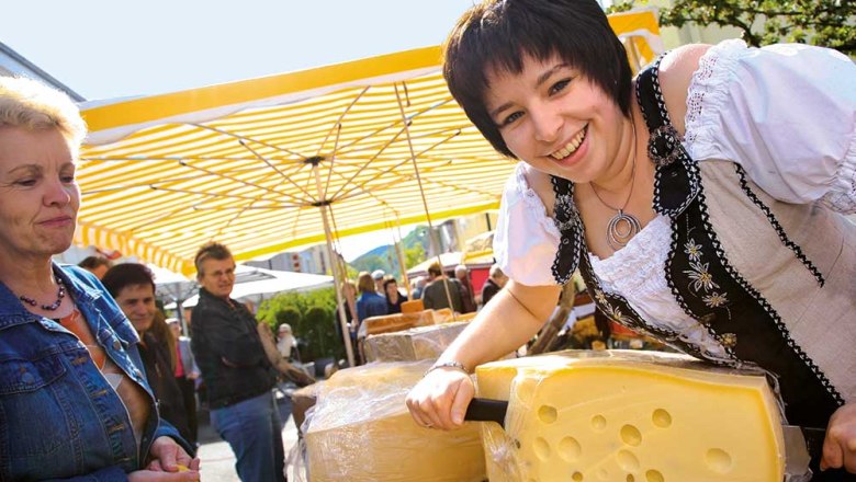 Woman in traditional dress cutting cheese at a market.