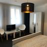 Modern furnished double room with bed, wardrobe, two chairs, small table and TV.