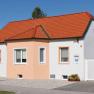 A small, single-storey house with an orange roof and white façade under a blue sky.
