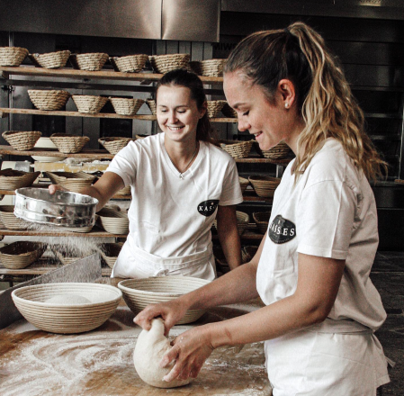 Two women are baking in a bakery and kneading dough.