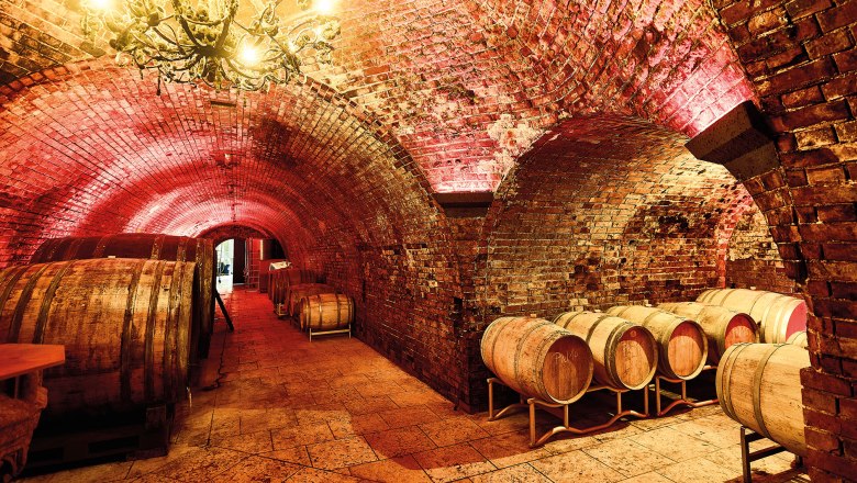 A wine cellar with brick vaults, wooden barrels and a chandelier.