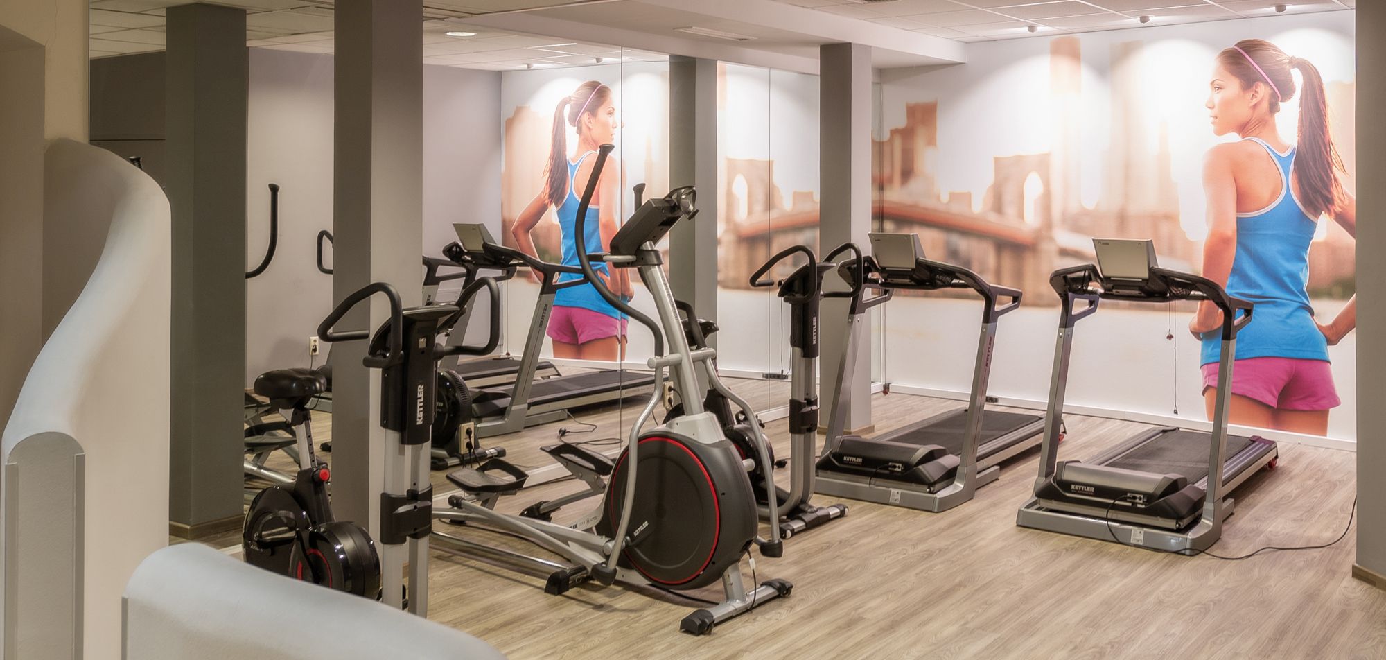 Fitness room with treadmills and fitness equipment, mural of a woman running.