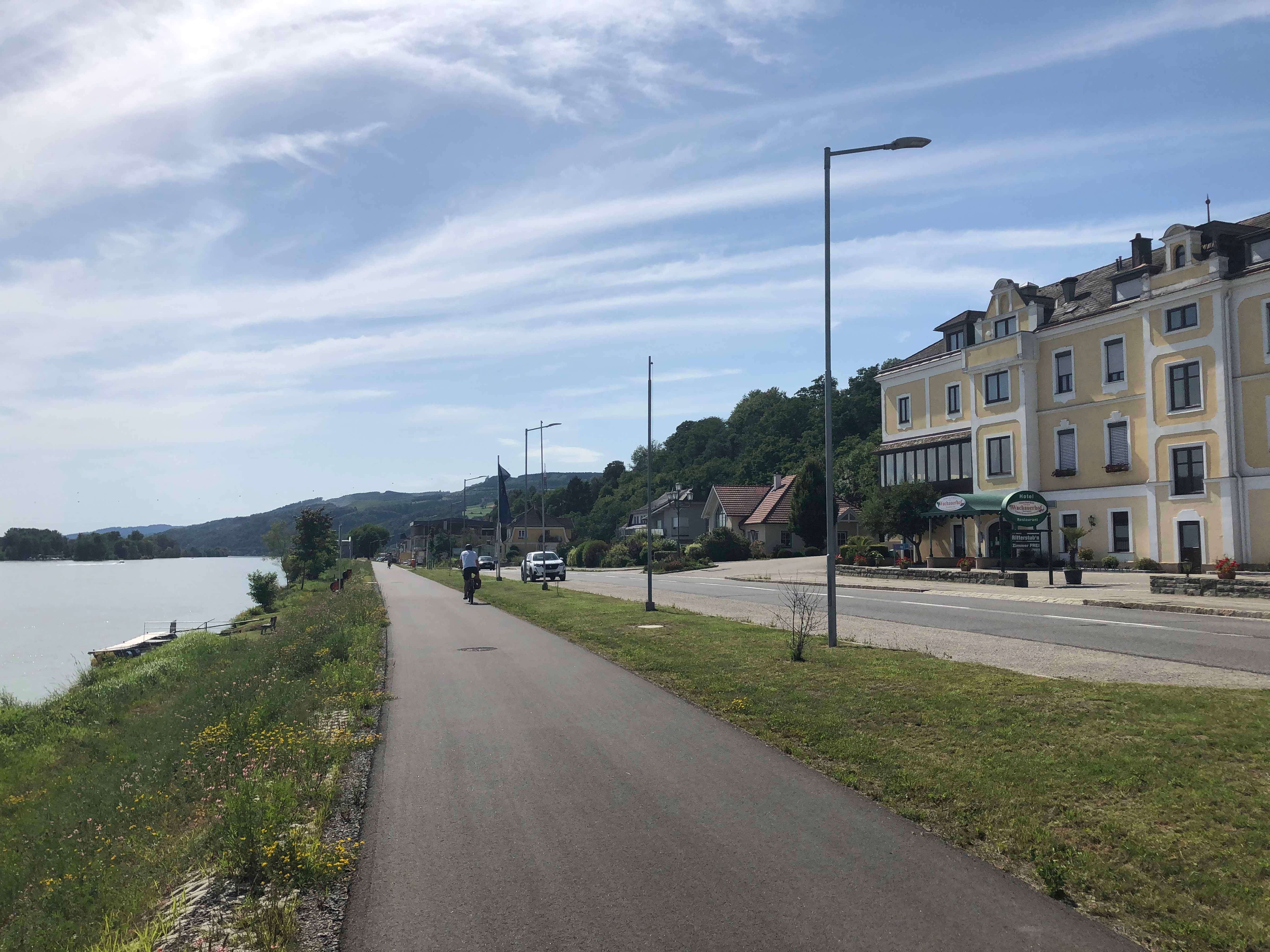 Street on the riverbank with yellow building and cyclist.