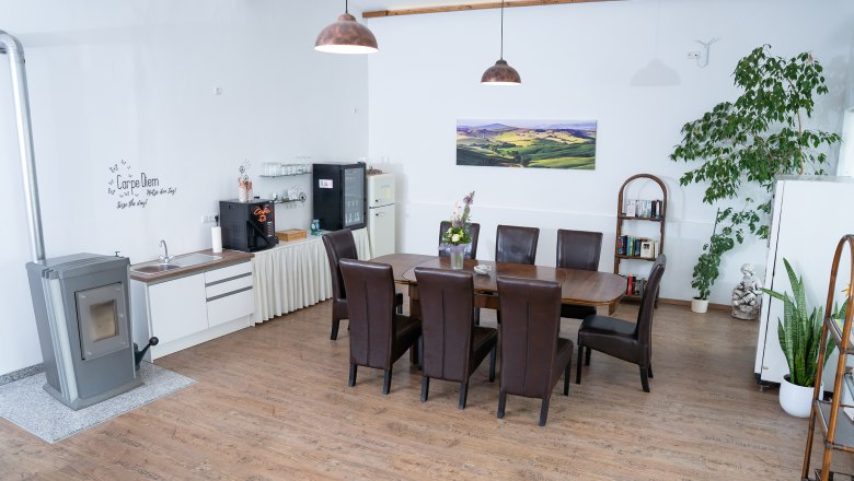Cozy room with dining table, chairs, plants and kitchenette.