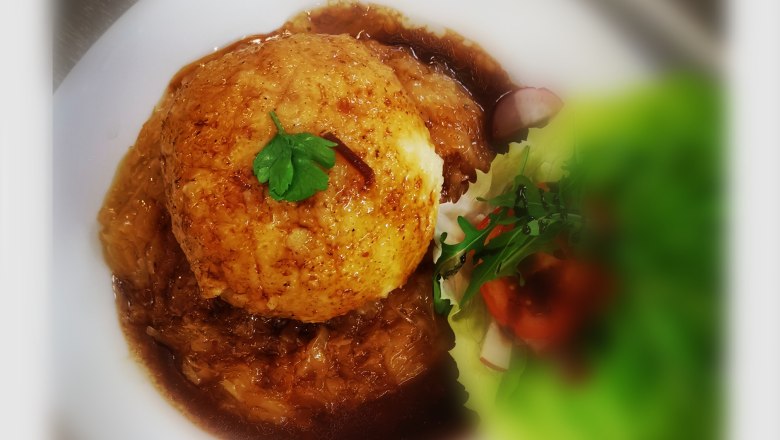 A plate with a large dumpling in gravy, garnished with parsley, and a salad with tomatoes and radishes.