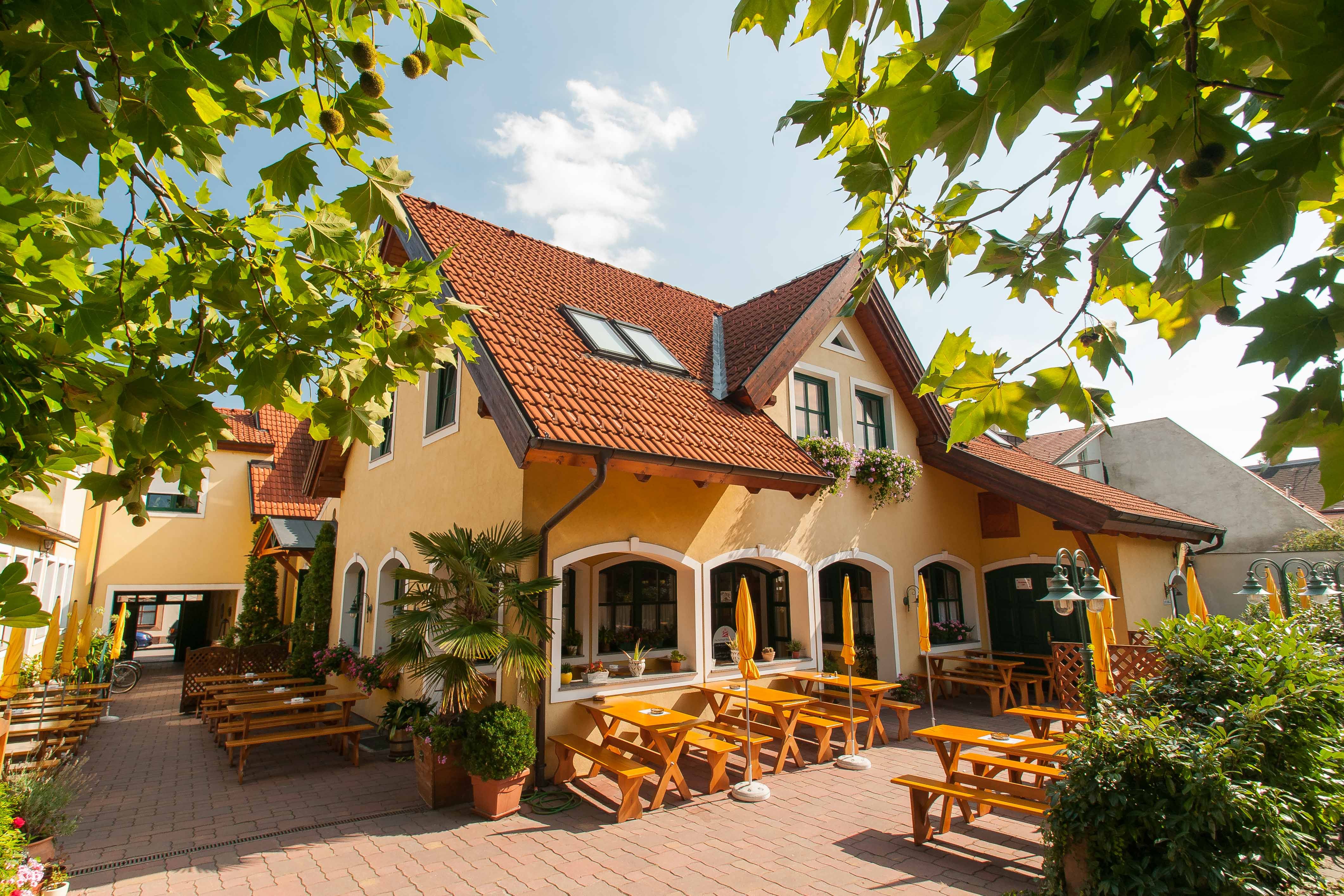 A yellow building with red roof tiles and a beer garden with wooden benches and parasols.