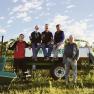 A family poses on a tractor trailer in a vineyard.