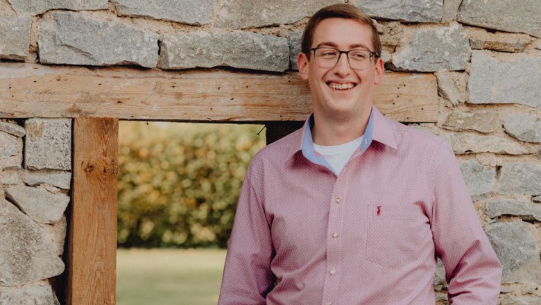 Man in pink shirt leaning against a stone wall.