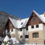 Snow-covered Villa Wellspacher in front of a wooded mountain in winter.