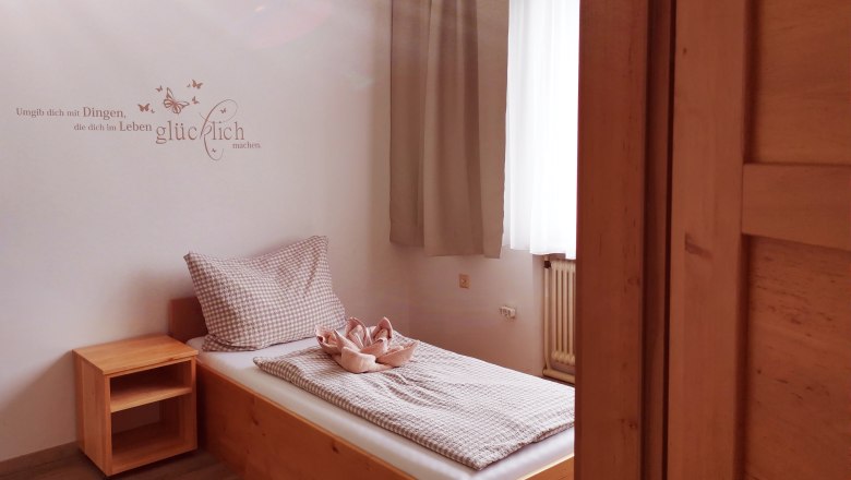 A simple guest room with a single bed, wooden shelf and a quote on the wall.
