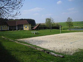Recreational area with volleyball court, meadow and buildings.