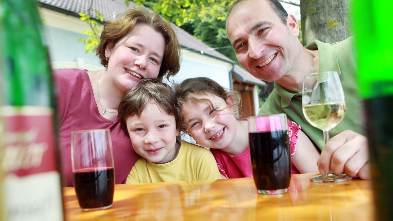 Family sitting at an outdoor table and smiling at the camera.