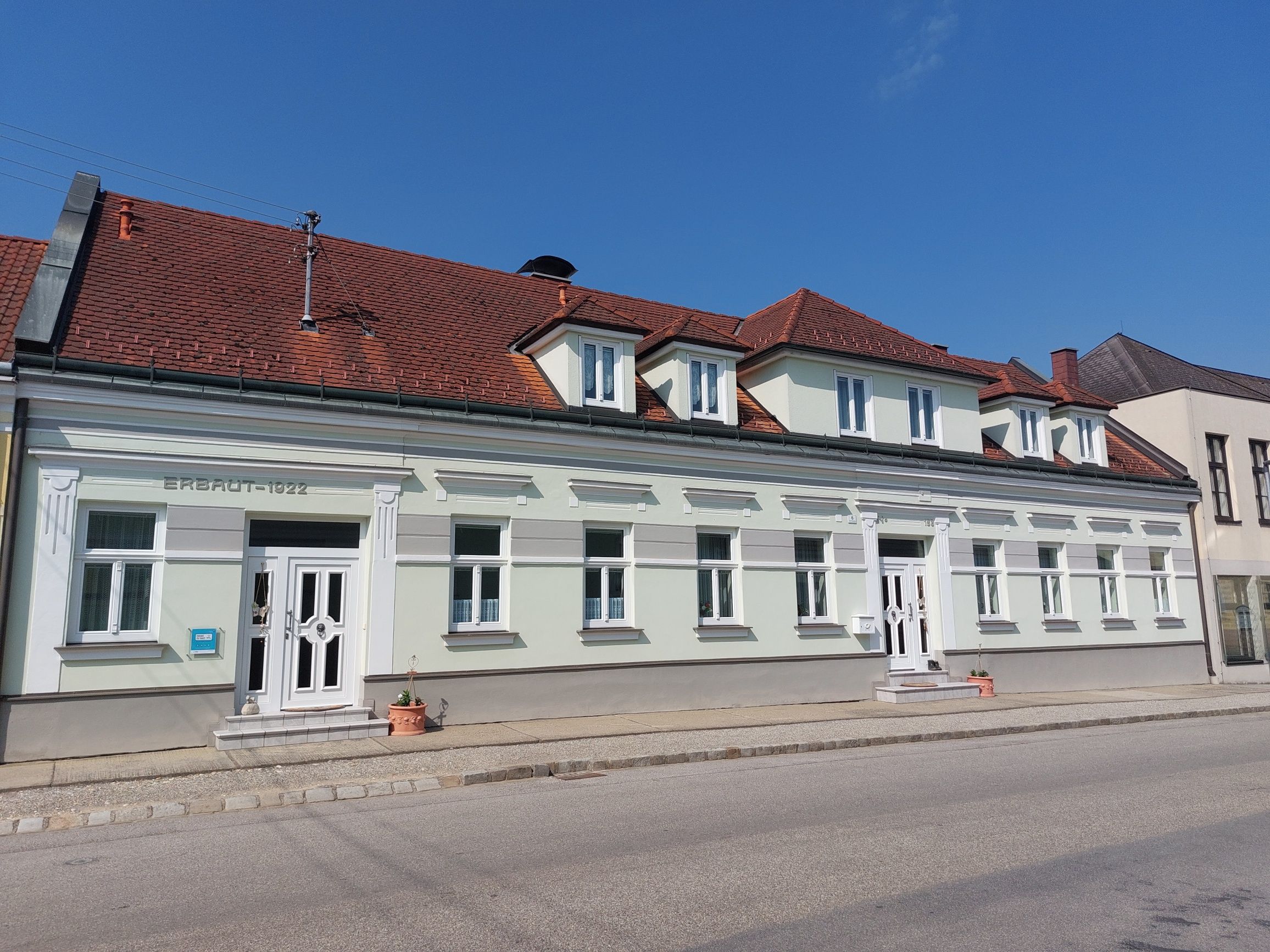A two-storey building with a red tiled roof and white window frames, built in 1922, in sunny weather.