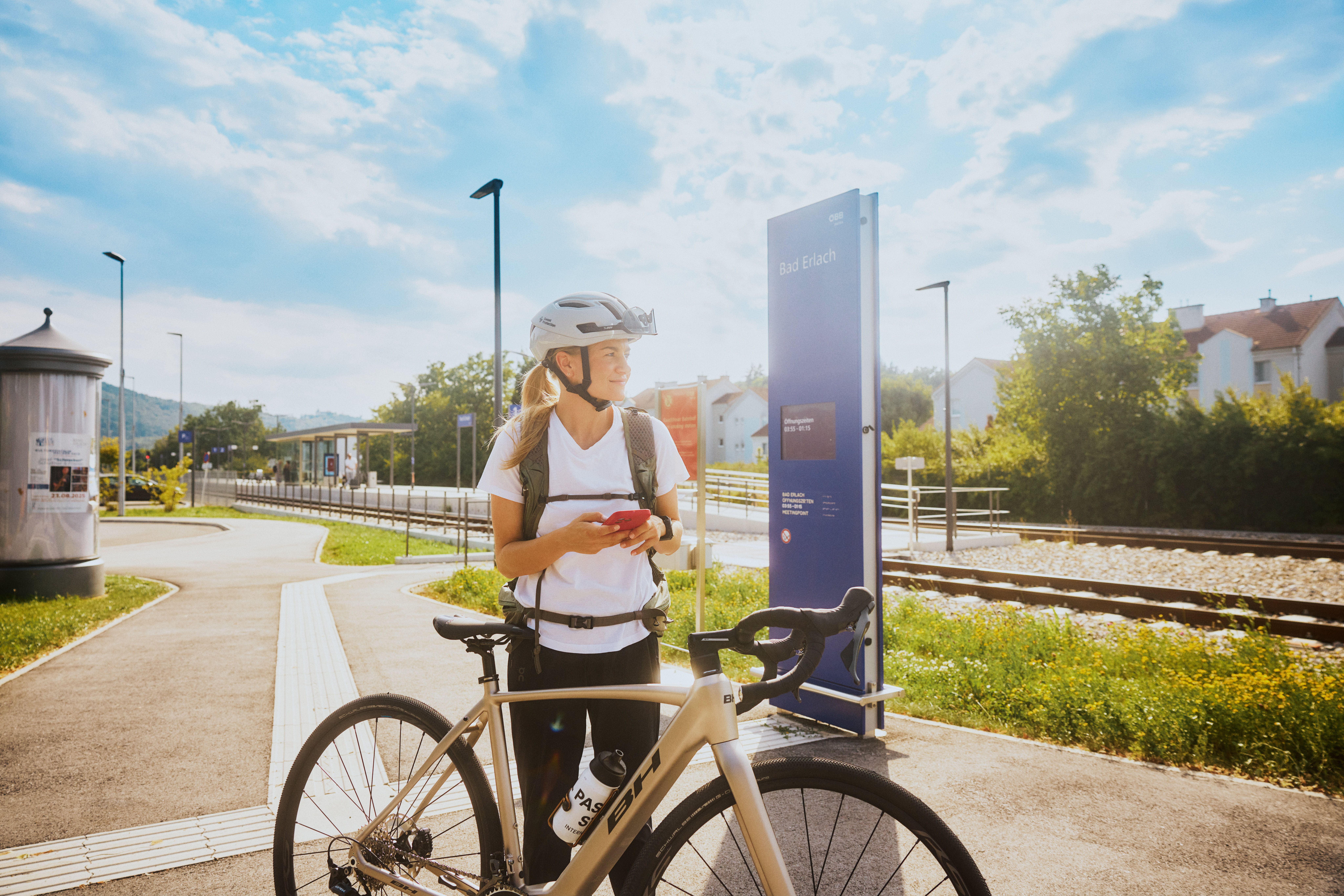 A woman with a bicycle helmet stands next to a bicycle at the train station in Bad Erlach.