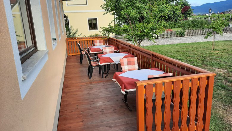 Wooden terrace with covered tables and chairs, surrounded by green landscape.
