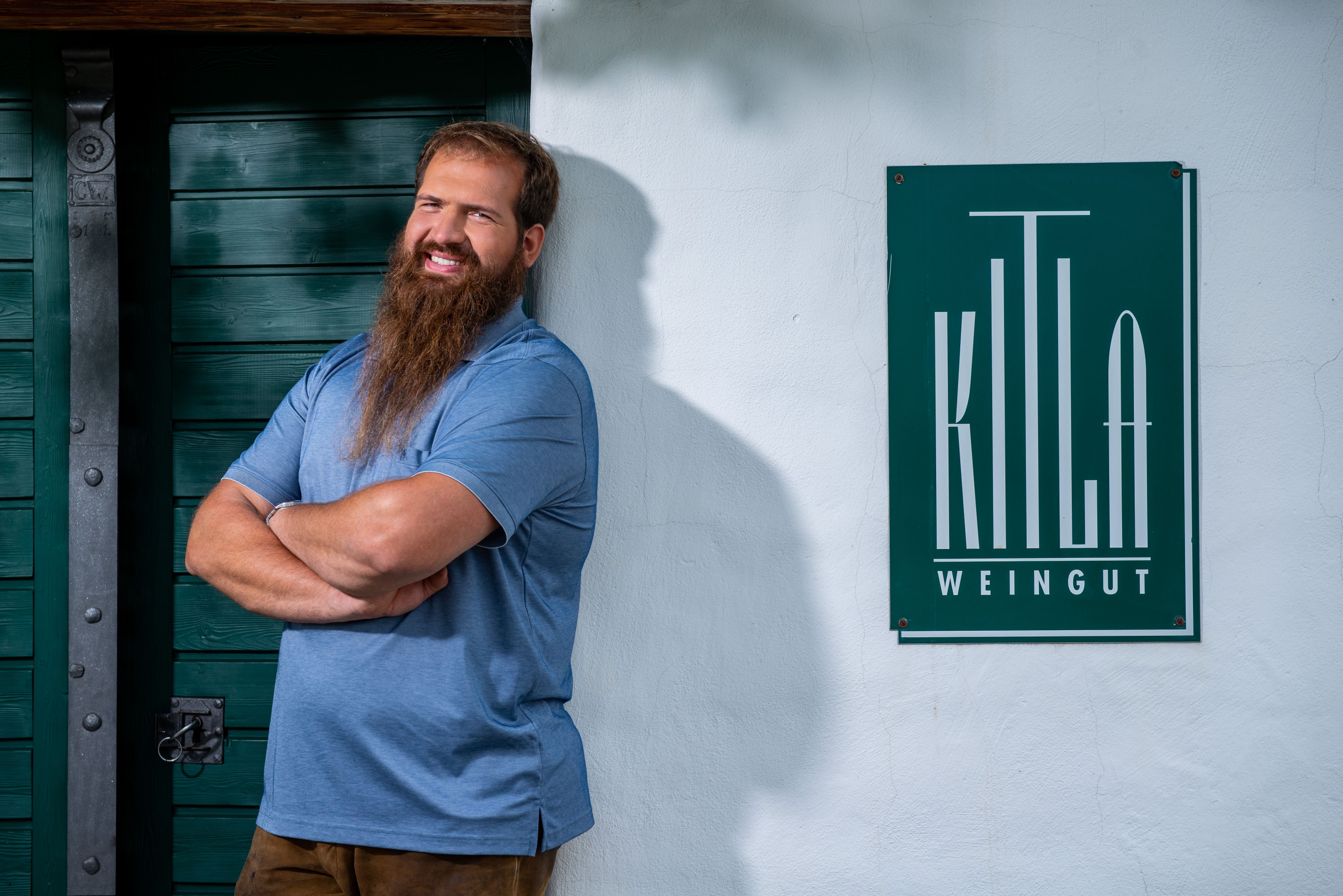 A man with a beard stands smiling in front of a sign that reads 'Kitla Winery'.