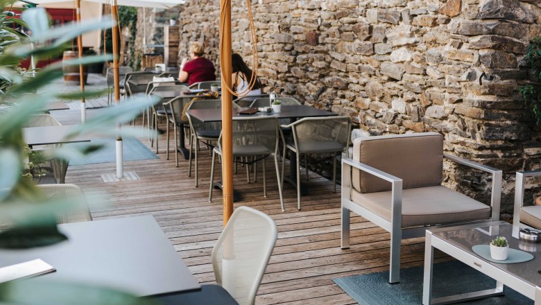 Cozy outdoor area of a caf&eacute; with wooden floor, modern furniture and stone wall.