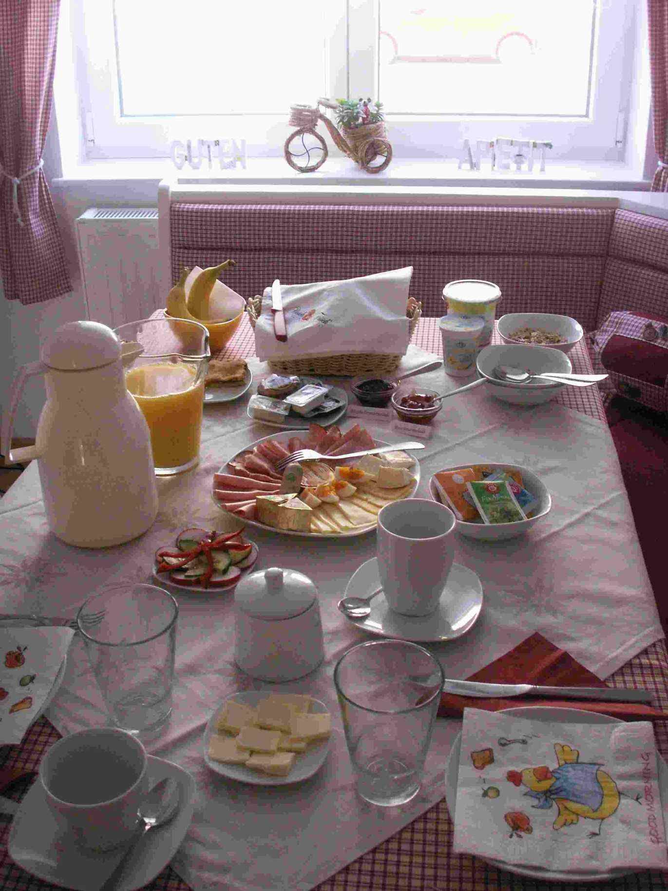 A laid breakfast table with bread rolls, cold cuts, cheese, juice and crockery.